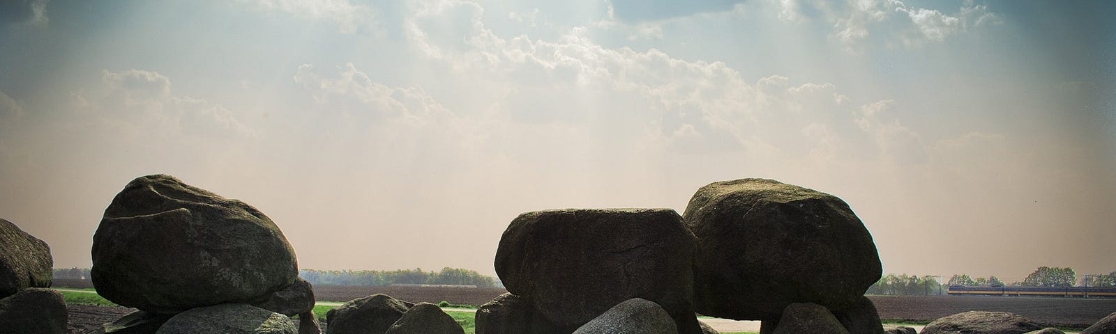 The sun shines down from a blue sky onto a circle of middle sized boulders, sitting on bright green grass.