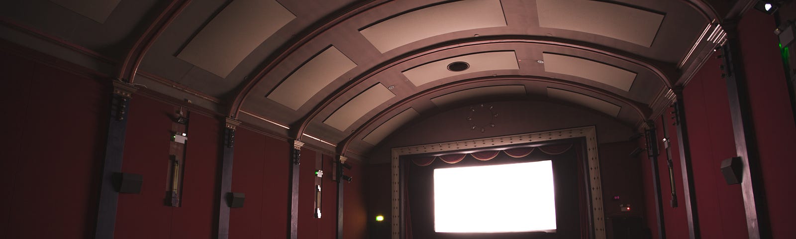 A full audience in the dark watching a giant movie screen way in the distance.