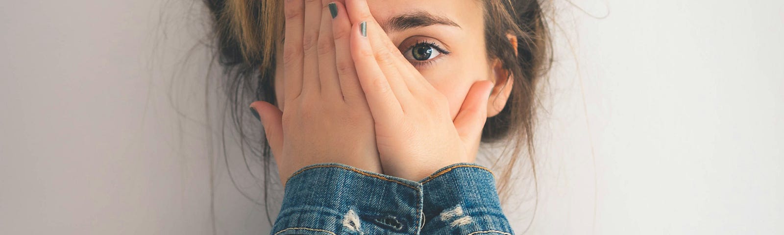 Scared young woman peeking through hands covering her face