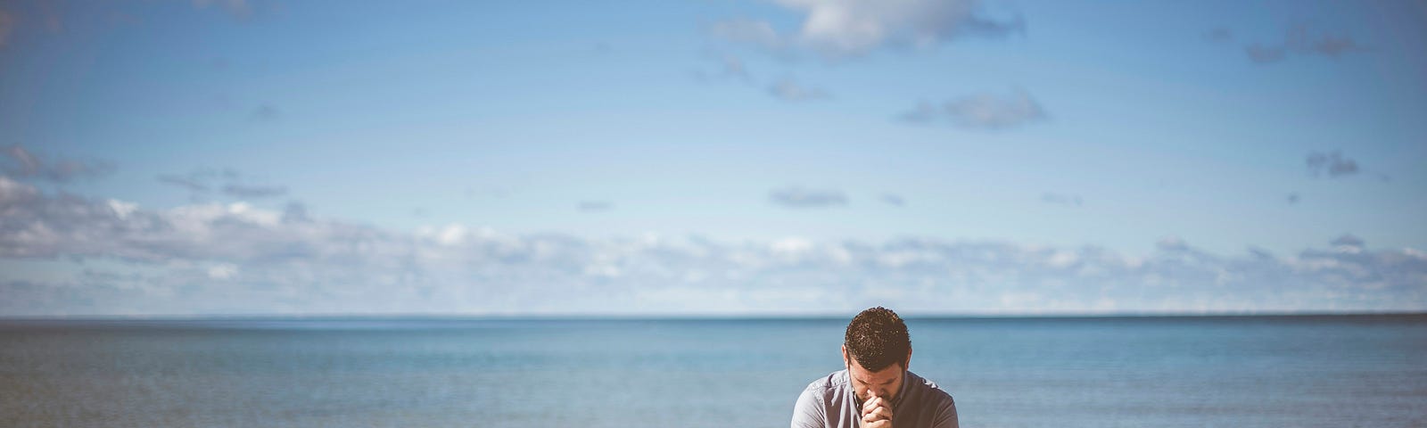 Man on beach kneeling in sand, praying.