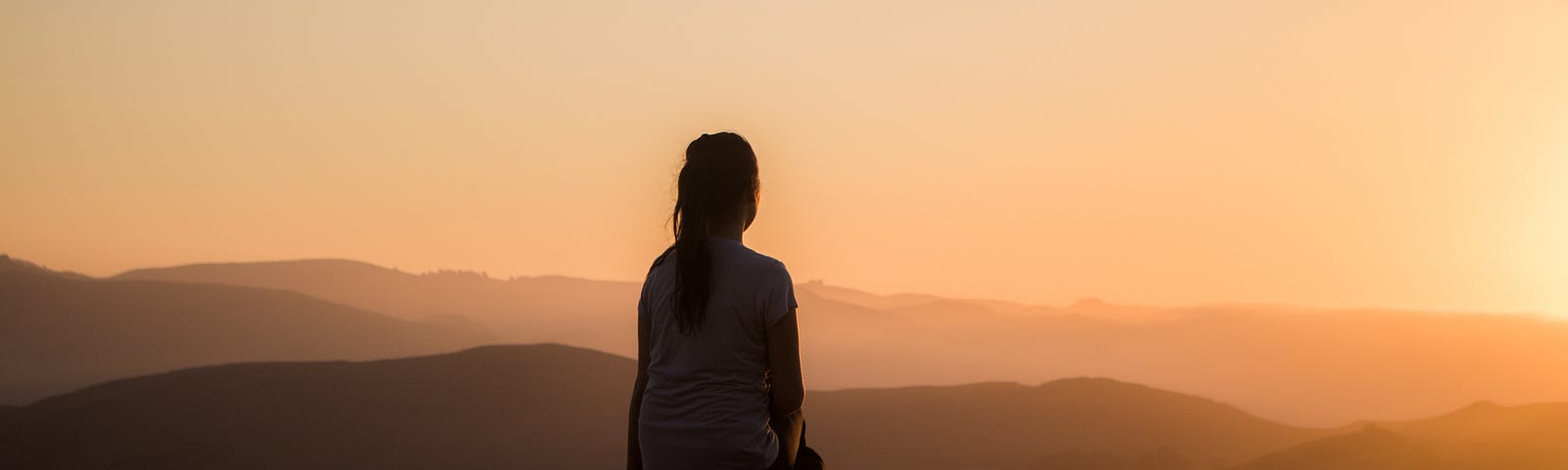 A picture of a young woman sitting on a bench and looking into the sunset in a beautiful mountainous area.