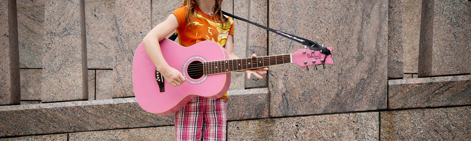 A red haired girl plays a pink guitar, singing her heart out on sidewalk venue!
