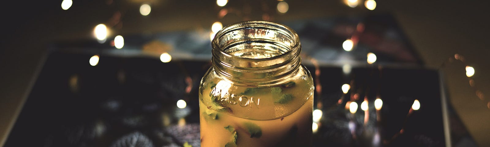 A jar of some herb concoction sits on a tray of leaves, with points of light hovering around it