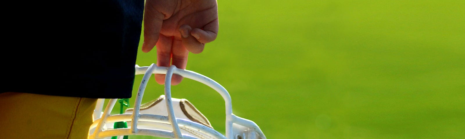 Photo of a football player holding a white football helmet that is dangling from two fingers.