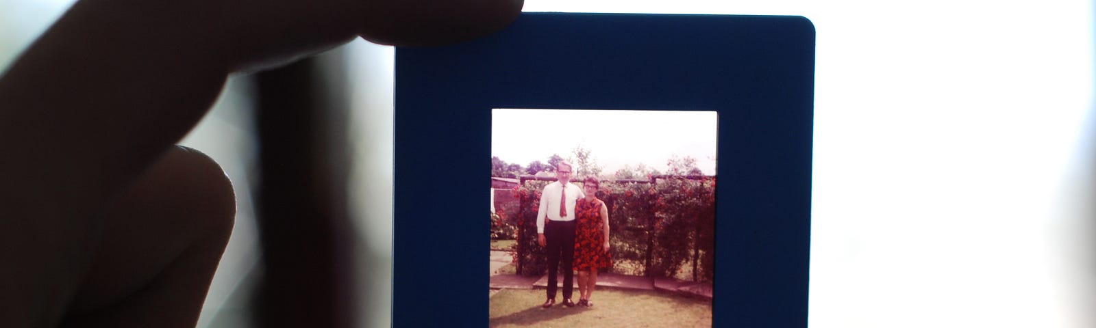 Close up of two digits holding a slide (depicting an older man and woman).