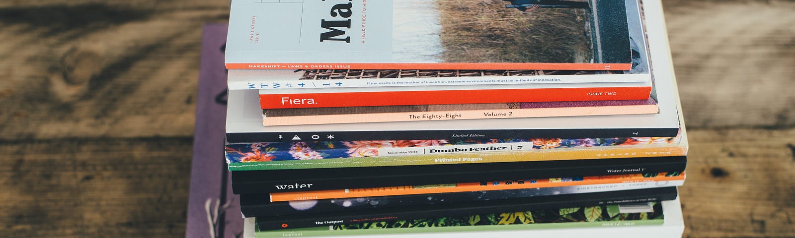 A stack of well-worn magazines sits on a wooden desk.