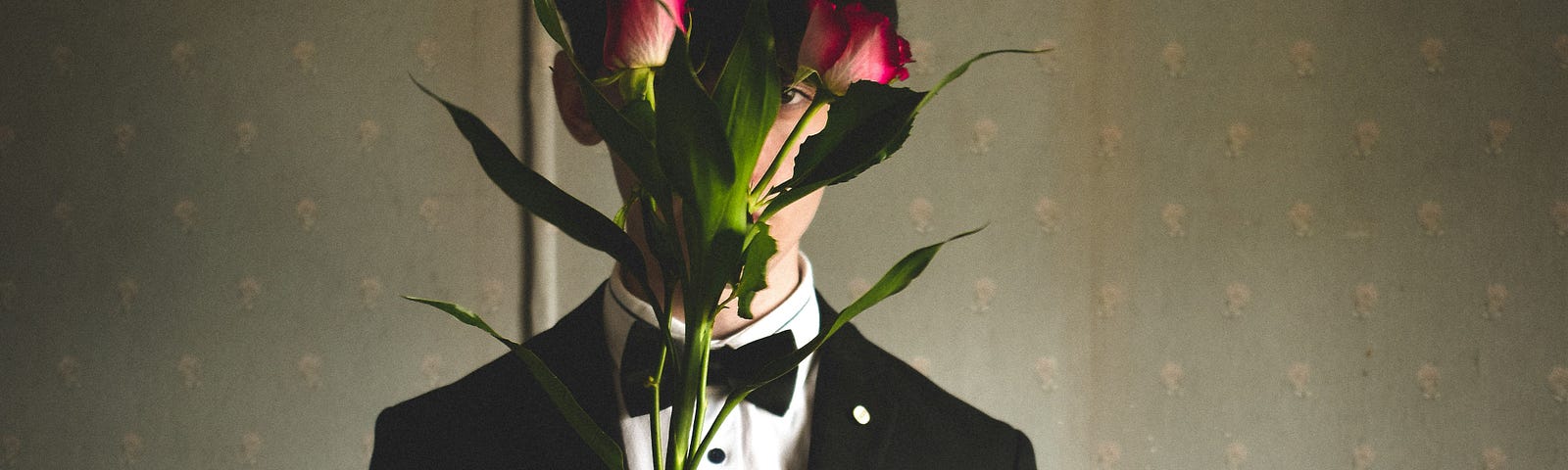 Foreground: A man in a tuxedo holds flowers that obscure his face. Background: An old faded yellow landline phone sits on a worn wooden table.