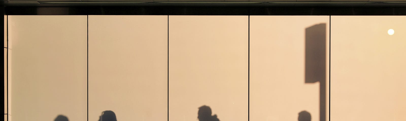 People silhouetted against the wall-to-wall windows of an office.