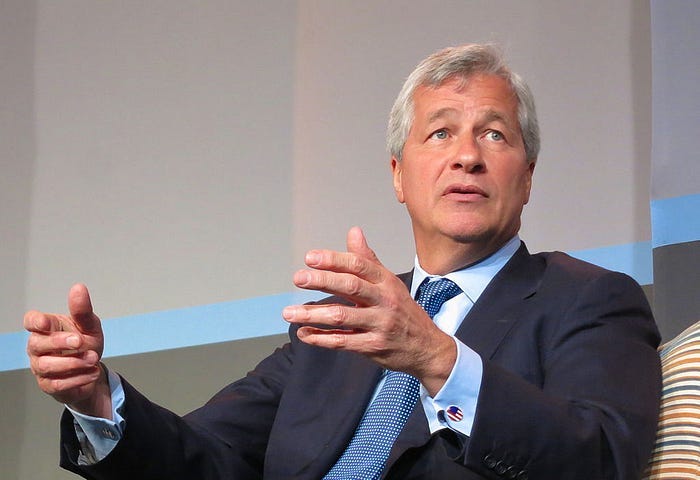 Jamie Dimon from JPMorgan Chase wearing a blue suit and patterned tie speaking and gesturing with his hands.