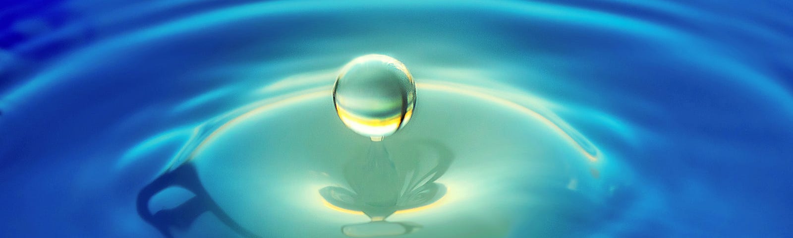 A droplet of water hovering over blue green water illustrating bitterness