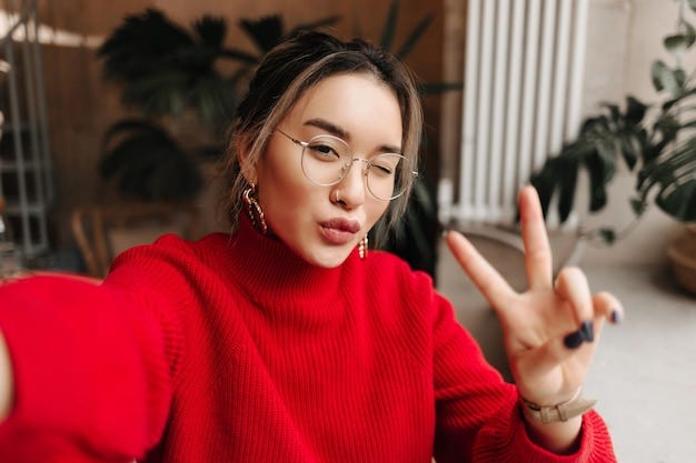 Young female blogger in bright sweater flashing the victory sign