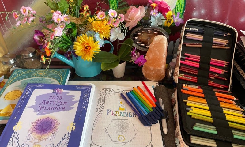 A set of books sits on a desk with an explosion of colourful pencils beside it and flowers behind it. You can’t hear it, but there’s relaxing music playing in the background as the smell of a warm tea wafts through the air.