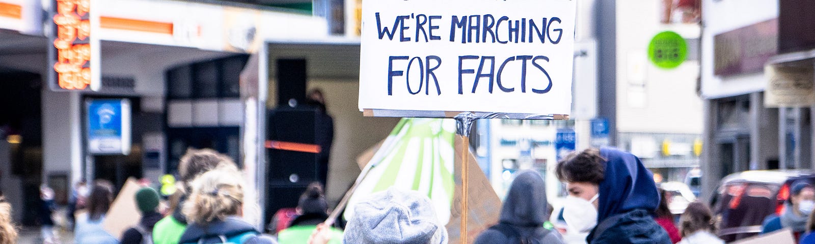 woman holding a sign that says “I can’t believe we’re marching for facts” at a protest march