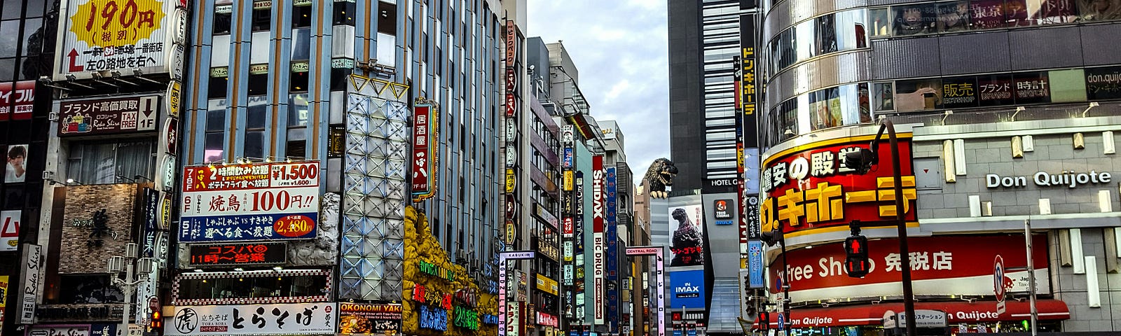 s street scene from Tokyo during the day. In the background, one of the buildings has a giant Godzilla billboard