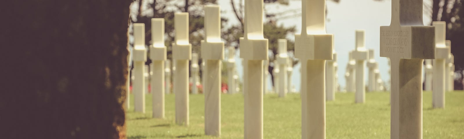 A row of cross-shaped tombstones, the closest of which has an American flag at its base