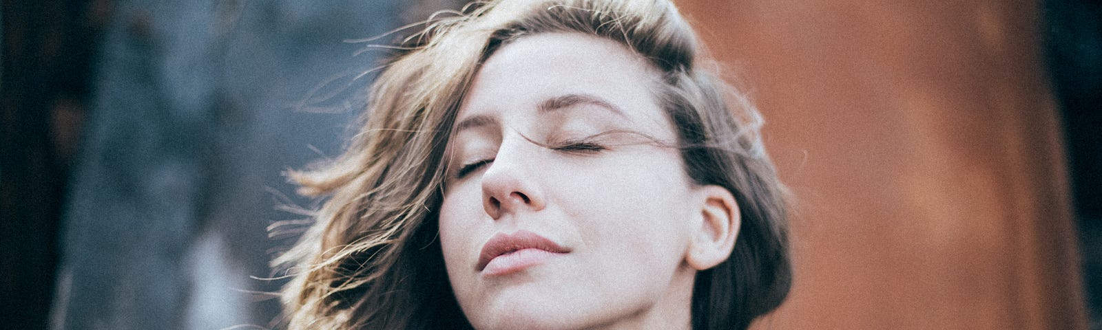 Woman with eyes closed and head pointed upwards, her brown hair is flowing in the wind.