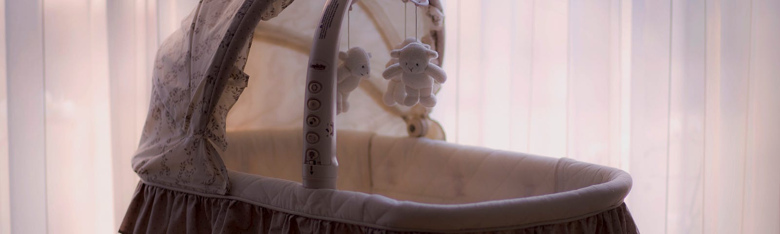 A bassinet that is not bright, can’t see if it’s empty or not; hanging mobile plush toys above it from its hood cover.