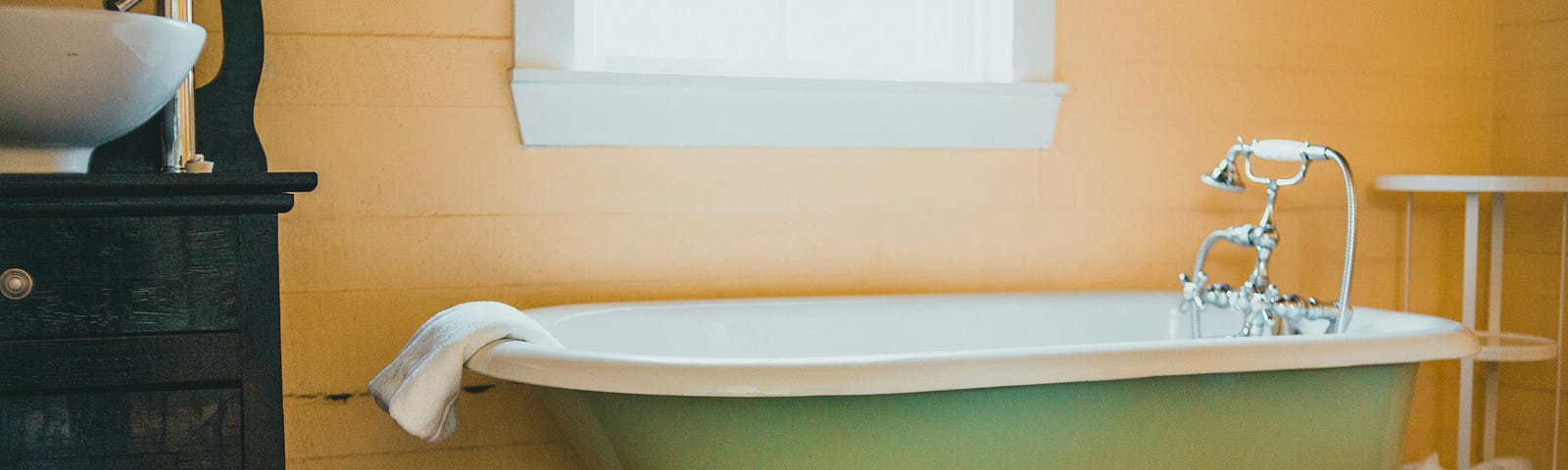 A photo of a clawfoot bathtub under a window and a bathoroom sink nearby.