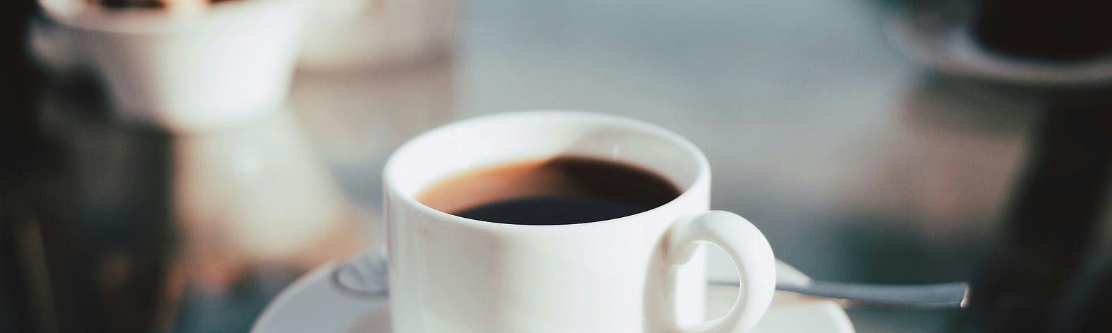 Coffe in a a white cup on top of a glass tabletop.