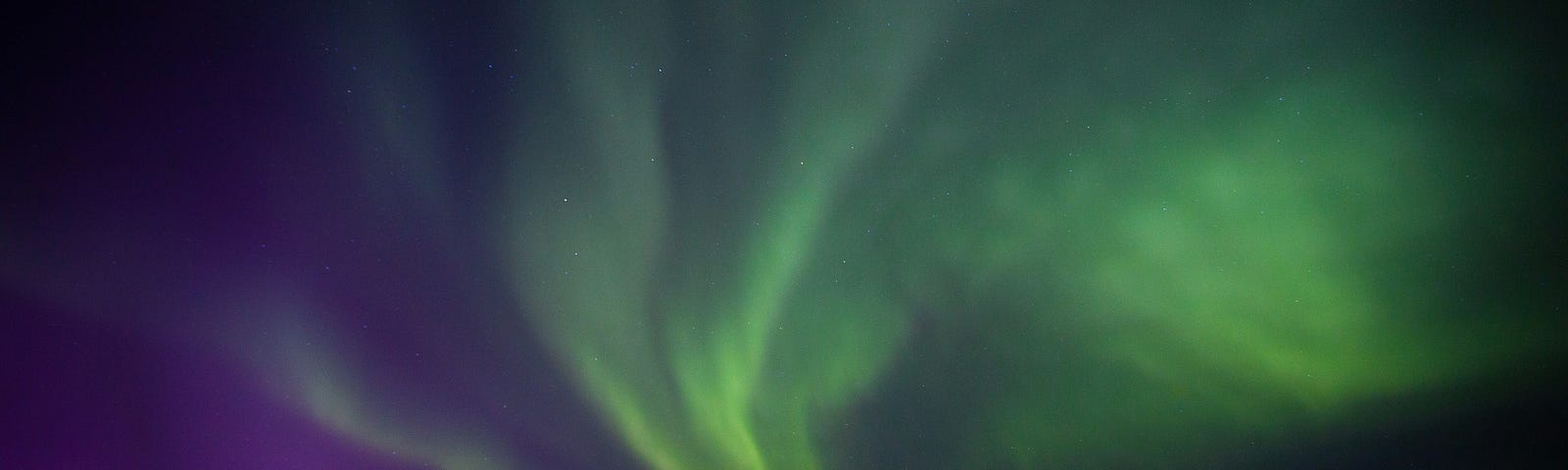 The Northern Lights in hues or green, yellow, and purple light the sky.