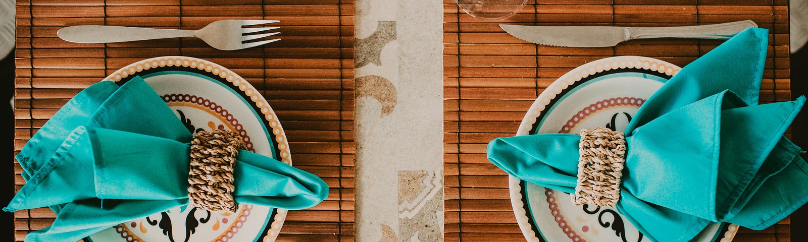 Top-down view of two table settings with teal napkins, plates, and knife and fork.