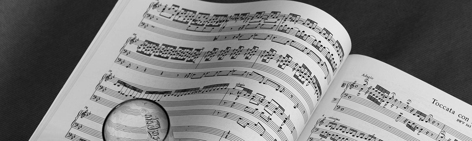 A book of sheet music opened with a pencil on the right page. An empty glass positioned beneath the left sheet.