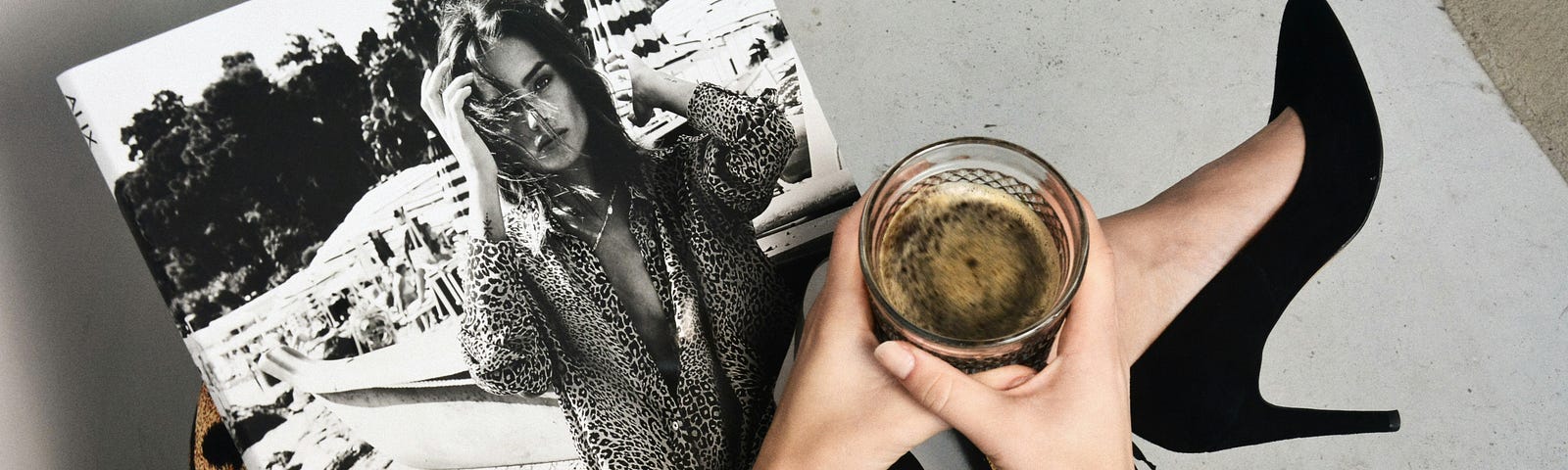 A woman wearing a stiletto looking at a magazine, with a cup of coffee in her hands.