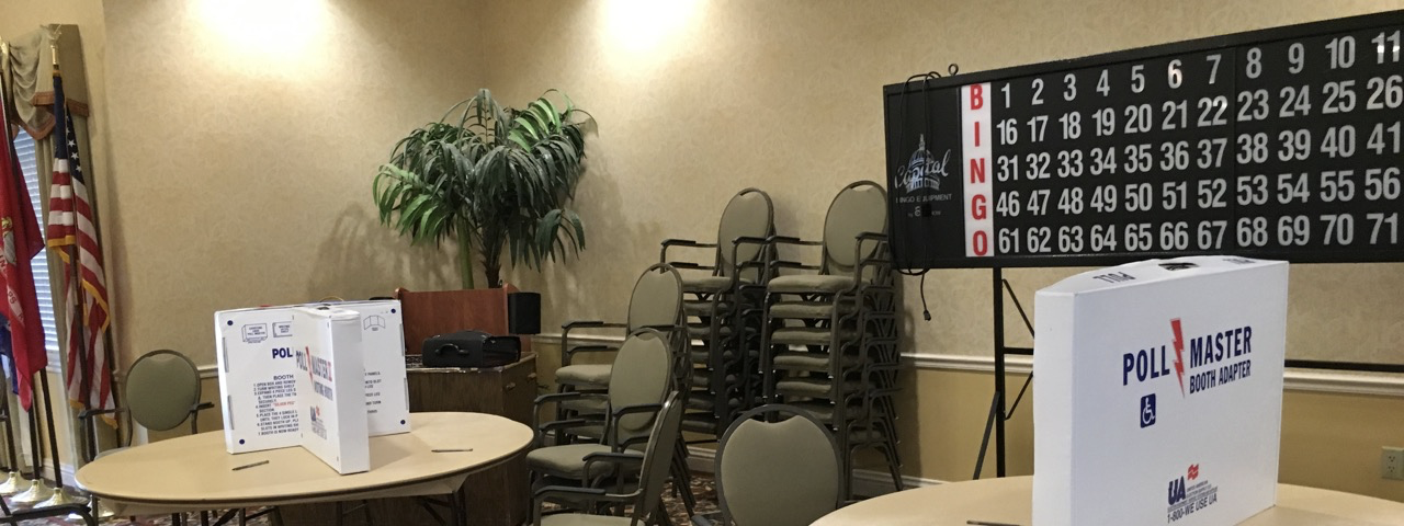 Large room with 2 round tables and boxes arranged to make privacy booths for voting