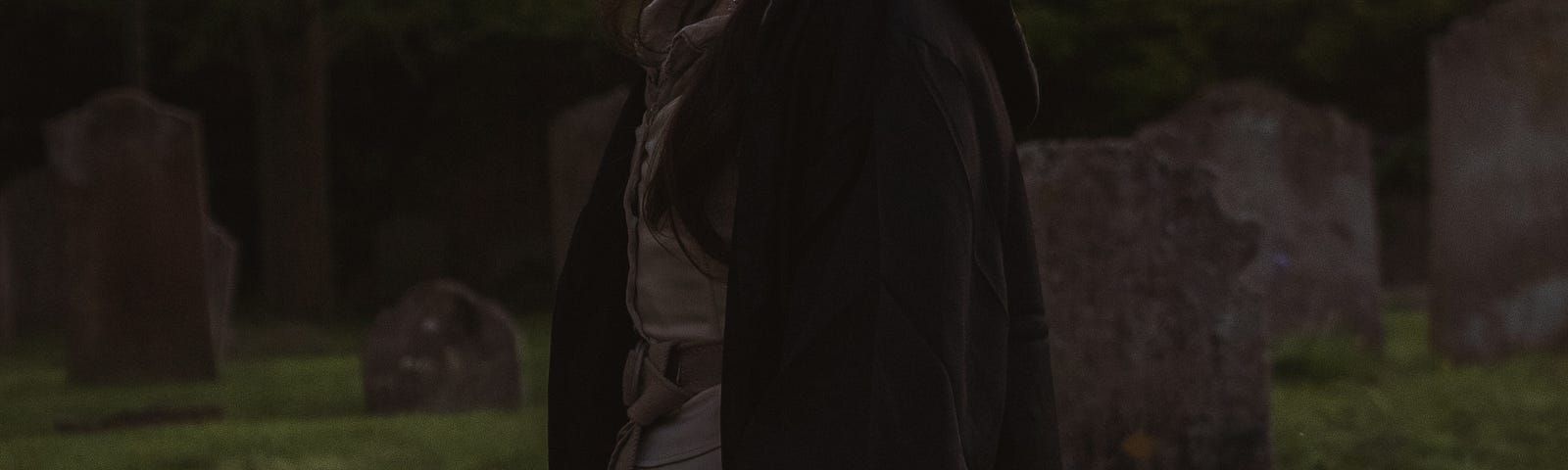 Olde-timey-dressed woman standing in a graveyard holding a sword