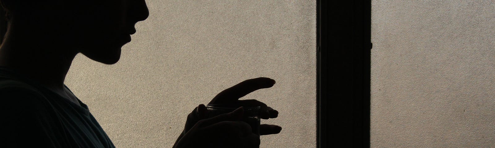 silhouette of a person holding a cup of tea or coffee, in front of a blurred window.