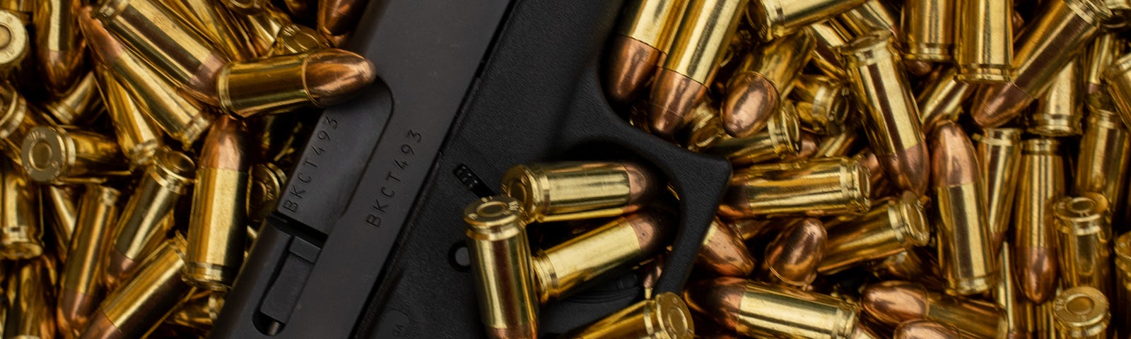 Black handgun laying in a pile of gold bullets.