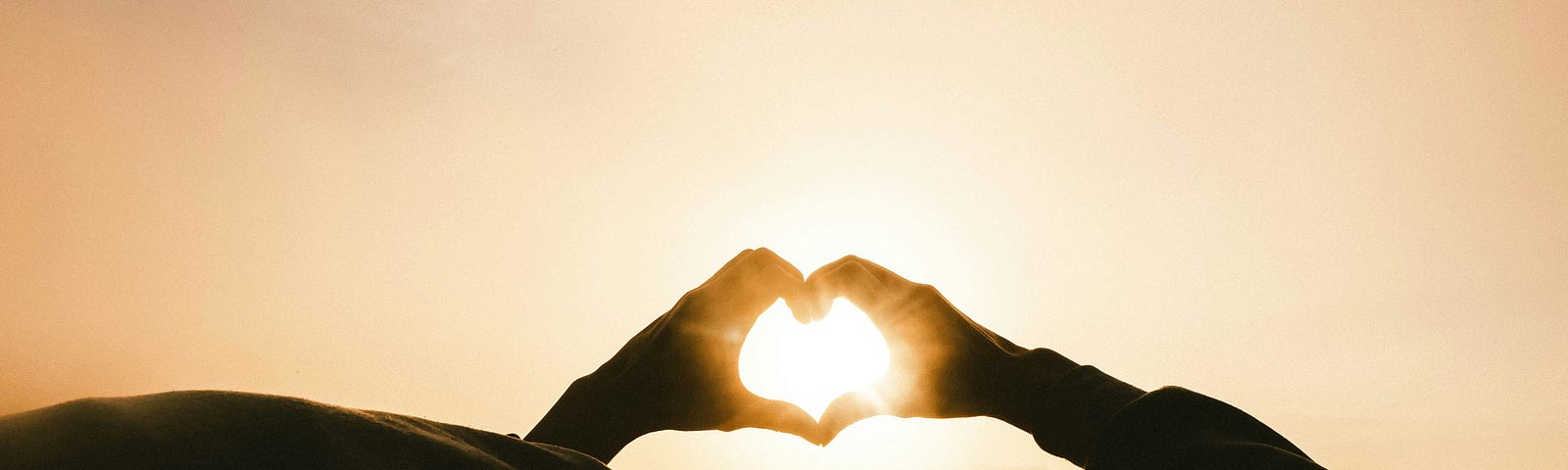 Hands forming a heart shape with sun glow in the background.