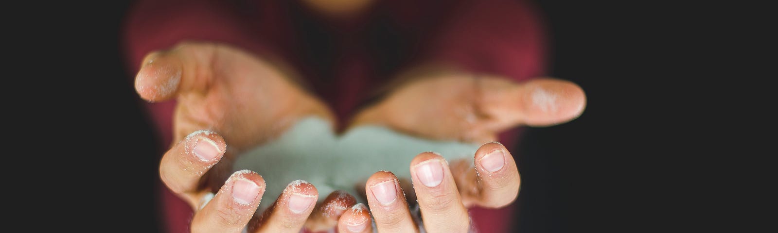 Man in a red shirt letting sand fall through his fingers