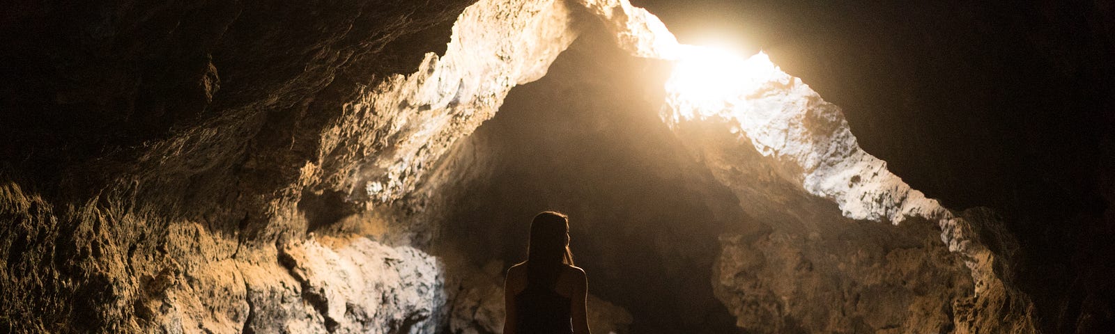 Woman standing in a cave where the light shines through a crack