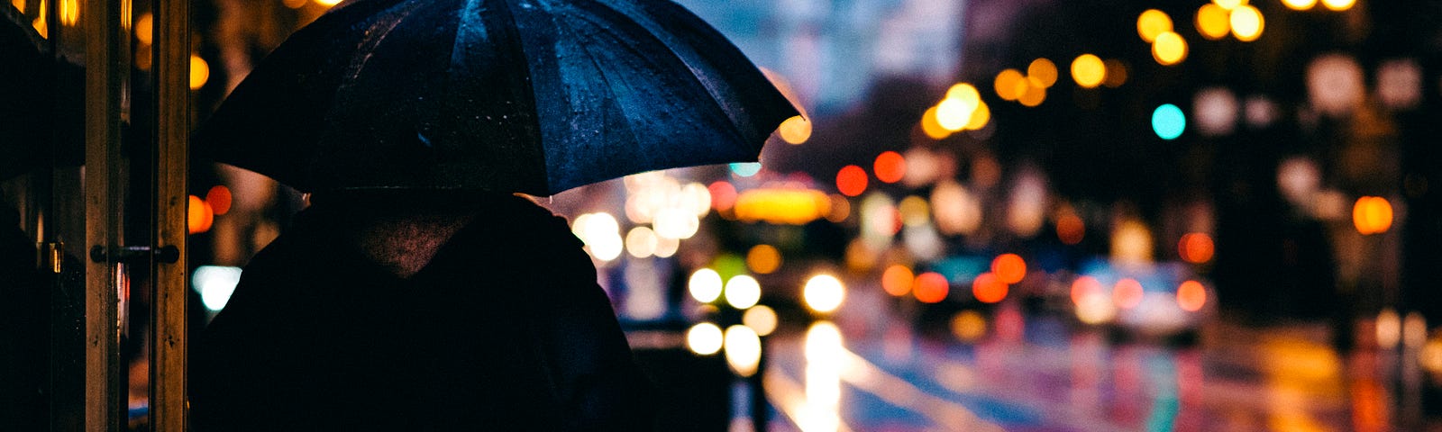 a silhouette of a person holding an umbrella in front of a rainy street with bright lights at night