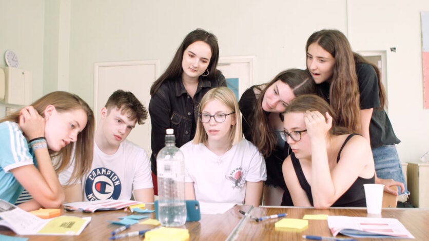 Young people gathered around a phone watching a film