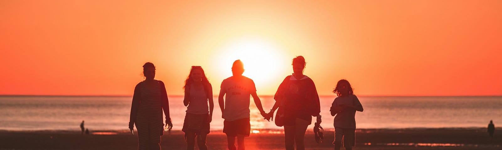 A family of people walk toward an ocean sunset.