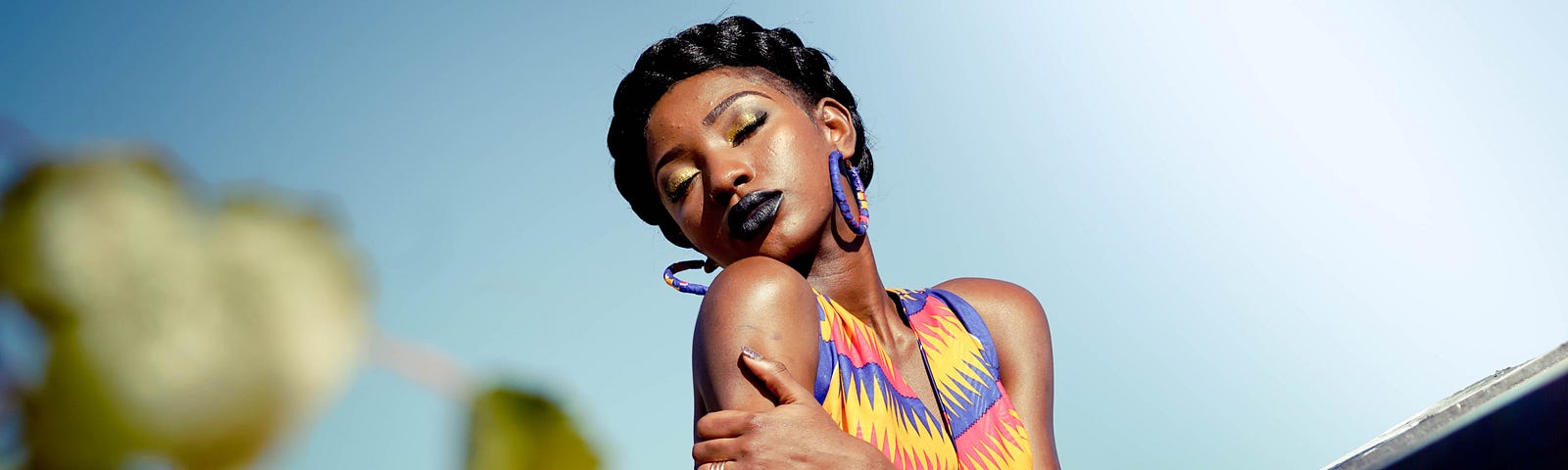 A gorgeous Black woman, braided hair and colorful dress, basks in the sun.