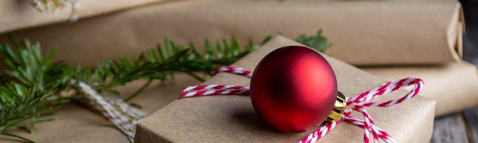 A pile of presents wrapped in brown paper and tied with red and white string and red baubles.