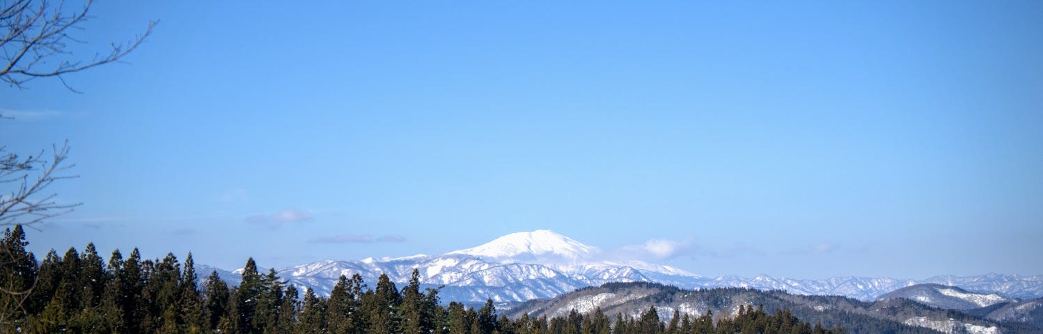 Forests in the foreground and a snowy Mt. Chokai sticking out in the background as seen from Mt. Yonetaihei in the middle of winter