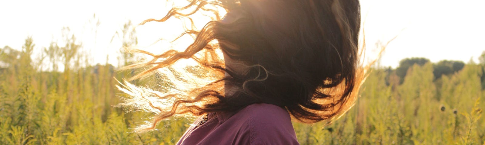 A young woman swings her hair up as the sun blazes in the background of a plant-filled field. Our breathing patterns may influence our ability to form memories. New groundbreaking research suggests the power of the breath: How it influences memory.