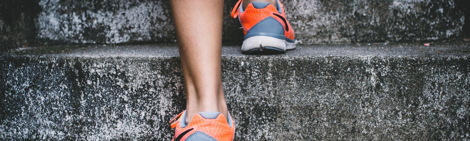 A close-up of the back side of a women in sneakers stepping up on a couple of concrete steps.