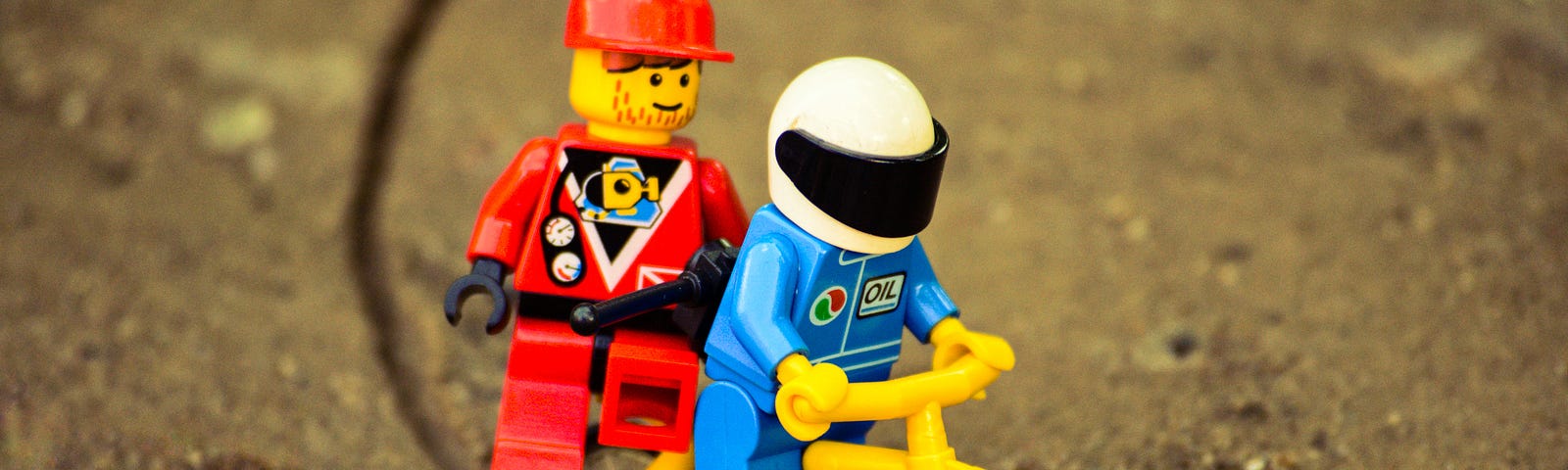 Two Lego man riding on a Lego bicycly. One is driving the other sits on the carrier.