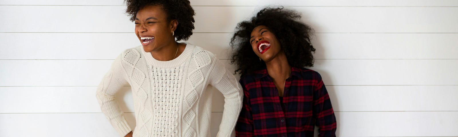 Two women standing in front of a wall, enjoying a good laugh together.