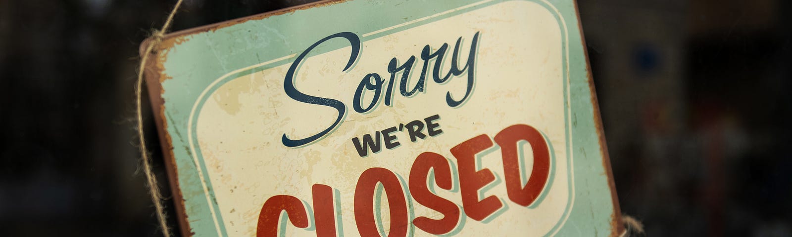 A sorry we’re closed sign hangs in a shop window.