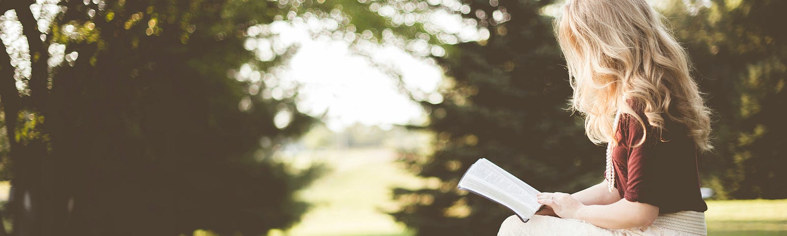 A woman reading a book outside in the sunshine.