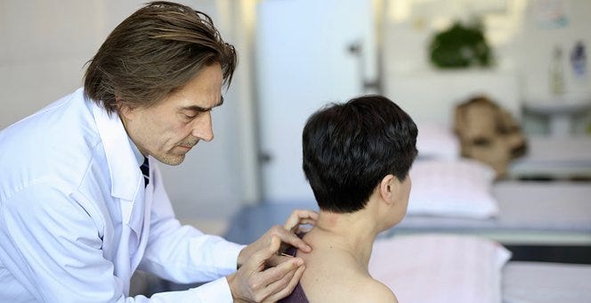 Doctor inserting acupuncture needle into a patient’s back
