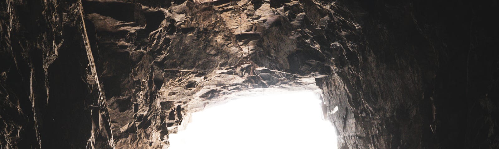 A cave tunnel with rock all around and white light shining at the far end.