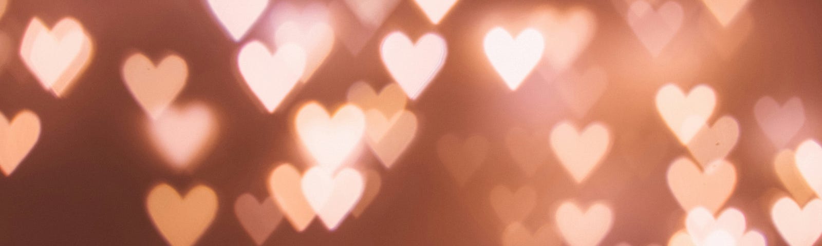 A brownish gold background filled with pale pink and white luminous hearts