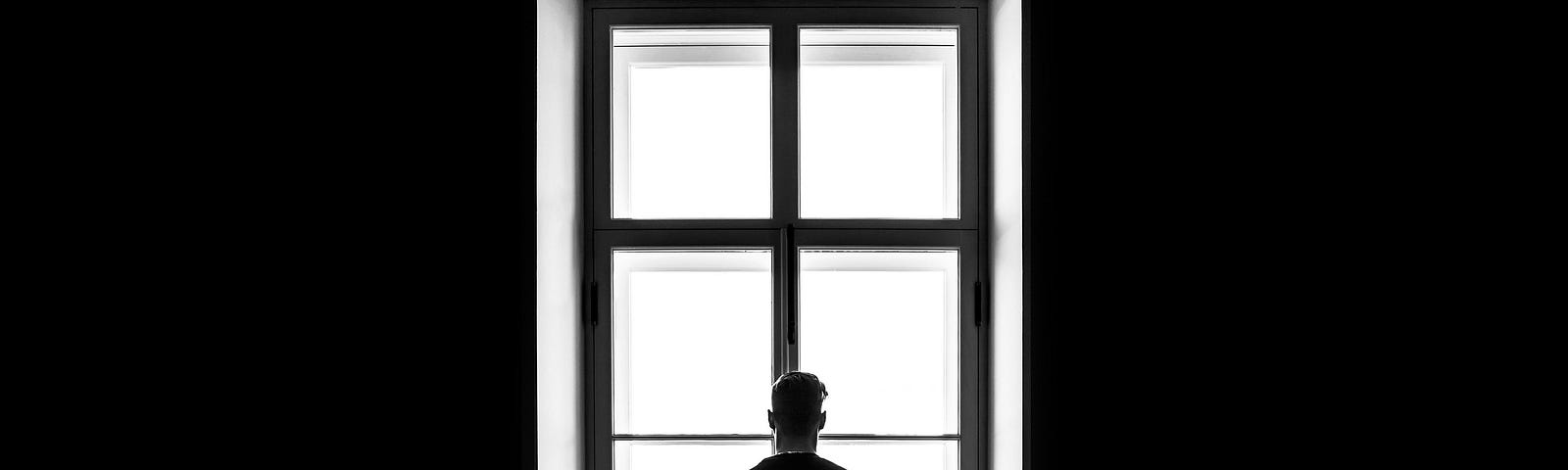Man standing at a window, staring straight ahead.